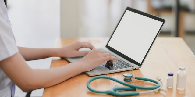 Laptop near teal stethoscope on wooden table