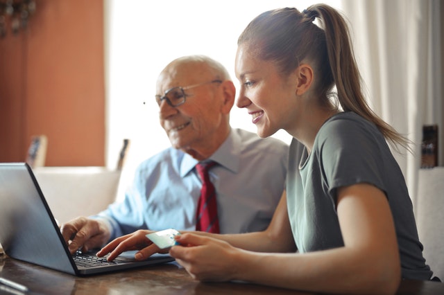 A young woman and an elderly man look at a laptop