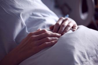 The hands of a patient in bed, resting their hands on their stomach